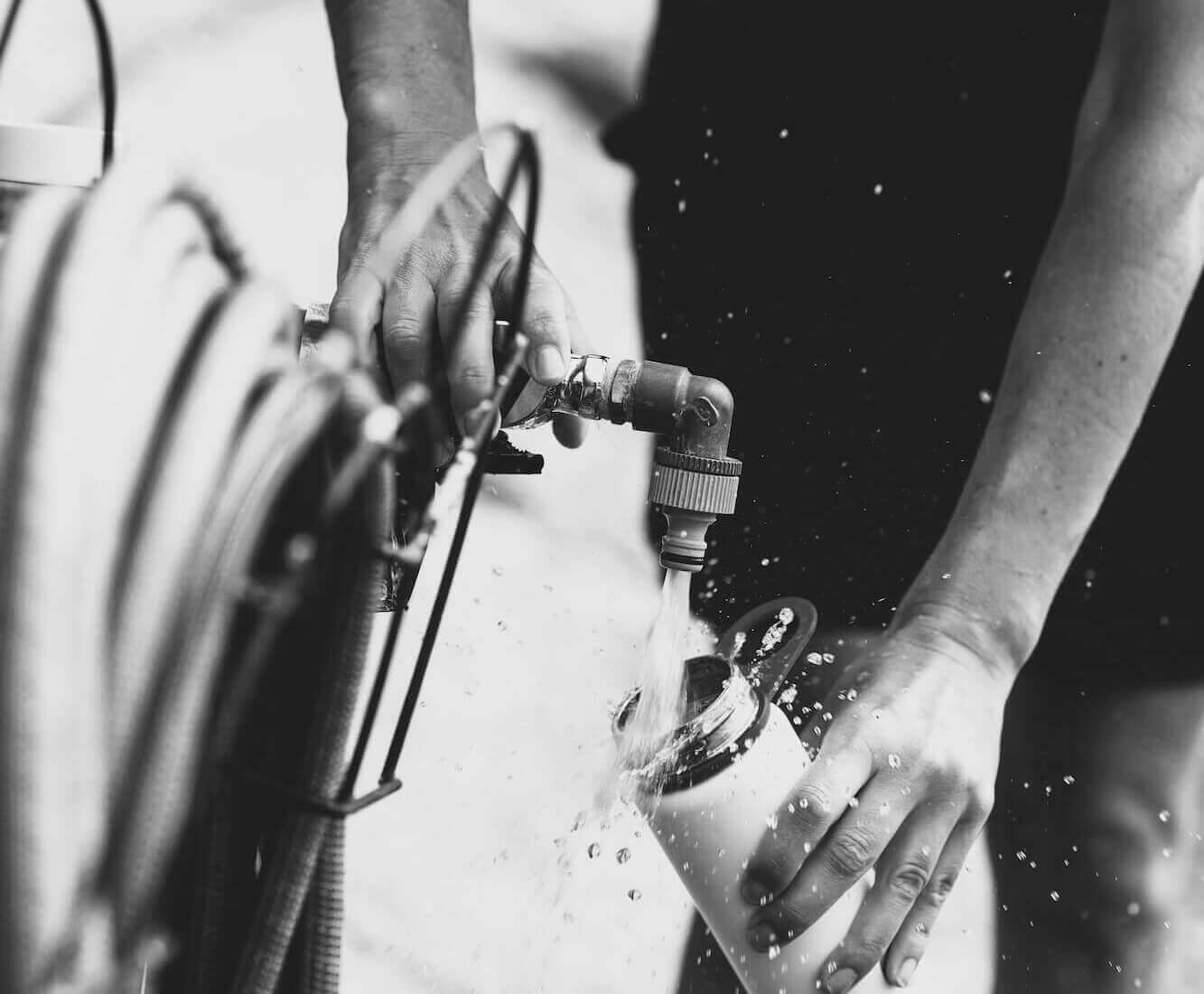 Plumber in Murray UT filling water container from outdoor faucet during plumbing service.